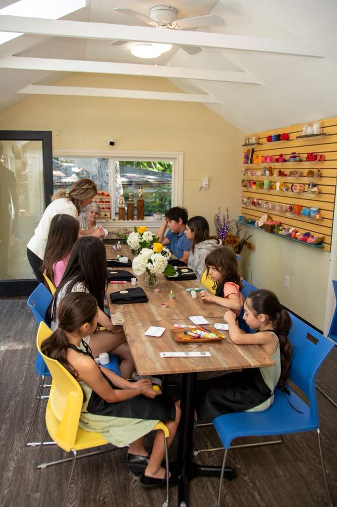 A long table of children in aprons painting candles in the Candle Art studio