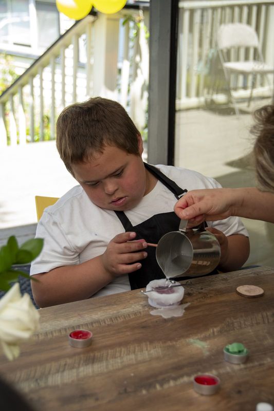 A boy tipping a steel pitcher of warm wax into his mold